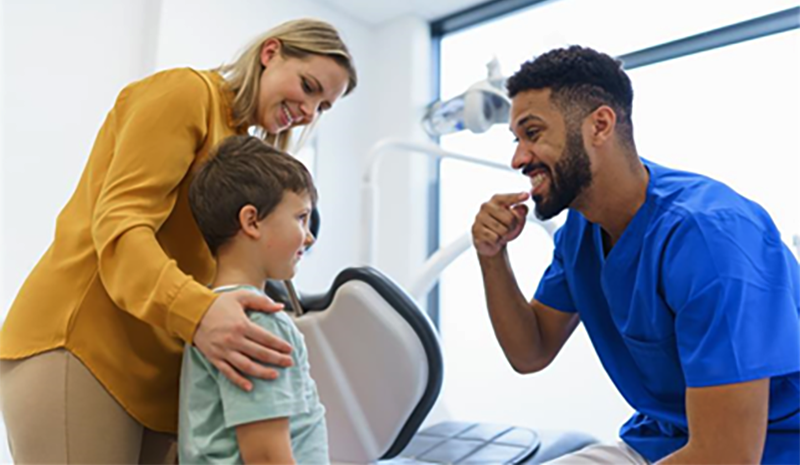 Dentist demonstrating how to clean your teeth to a young boy