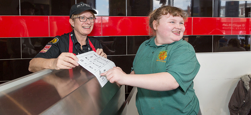 Girl choosing from a symbolised Chip Sheop menu, which is held by a female server